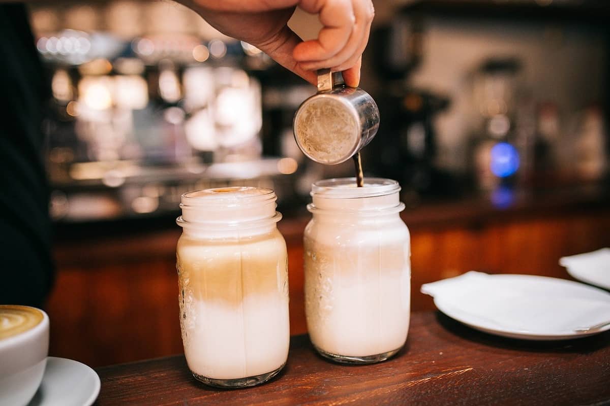 person pouring coffee into foamed milk jars