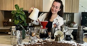 woman in a kitchen pouring into a V60 coffee brewer with a gooseneck kettle